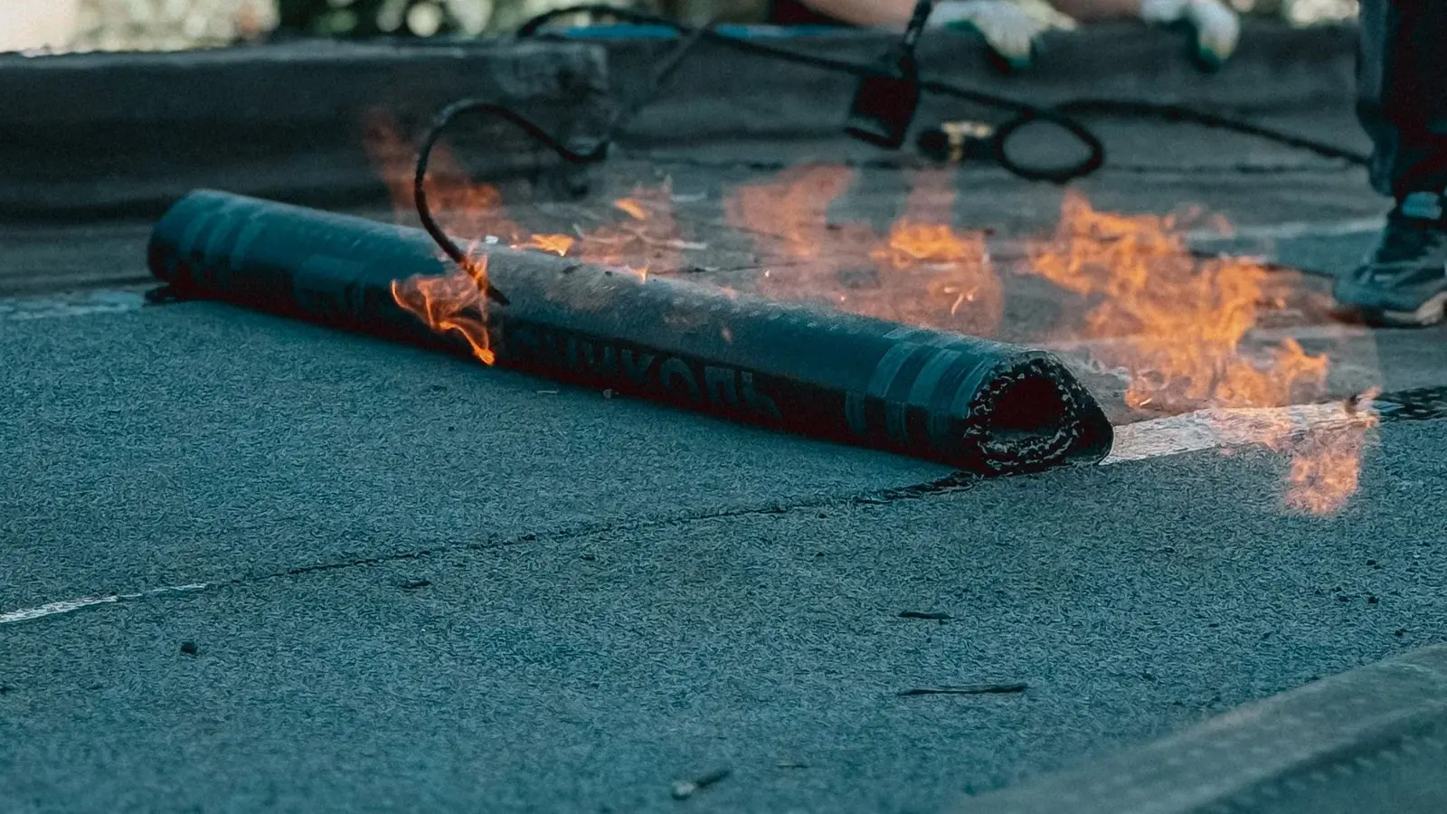 A roll of torch-down roofing membrane being heated on a flat roof