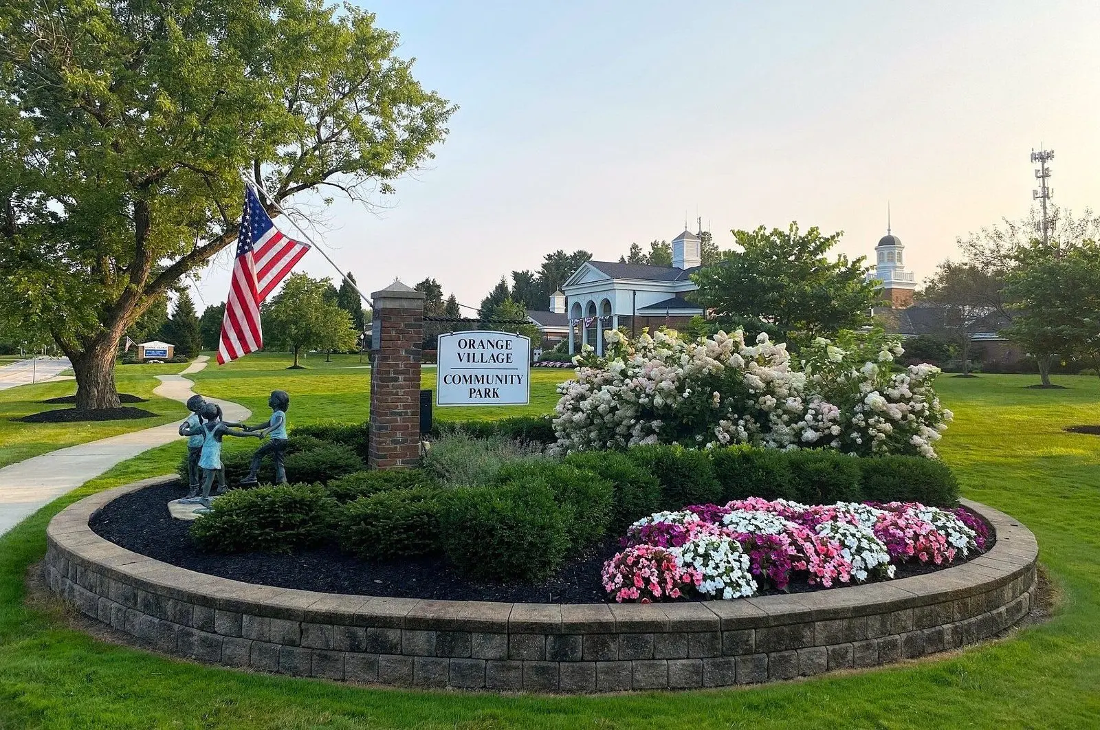 Flower bed and flag at the entrance to Orange Village Community Park, with the cupola-topped village buildings behind
